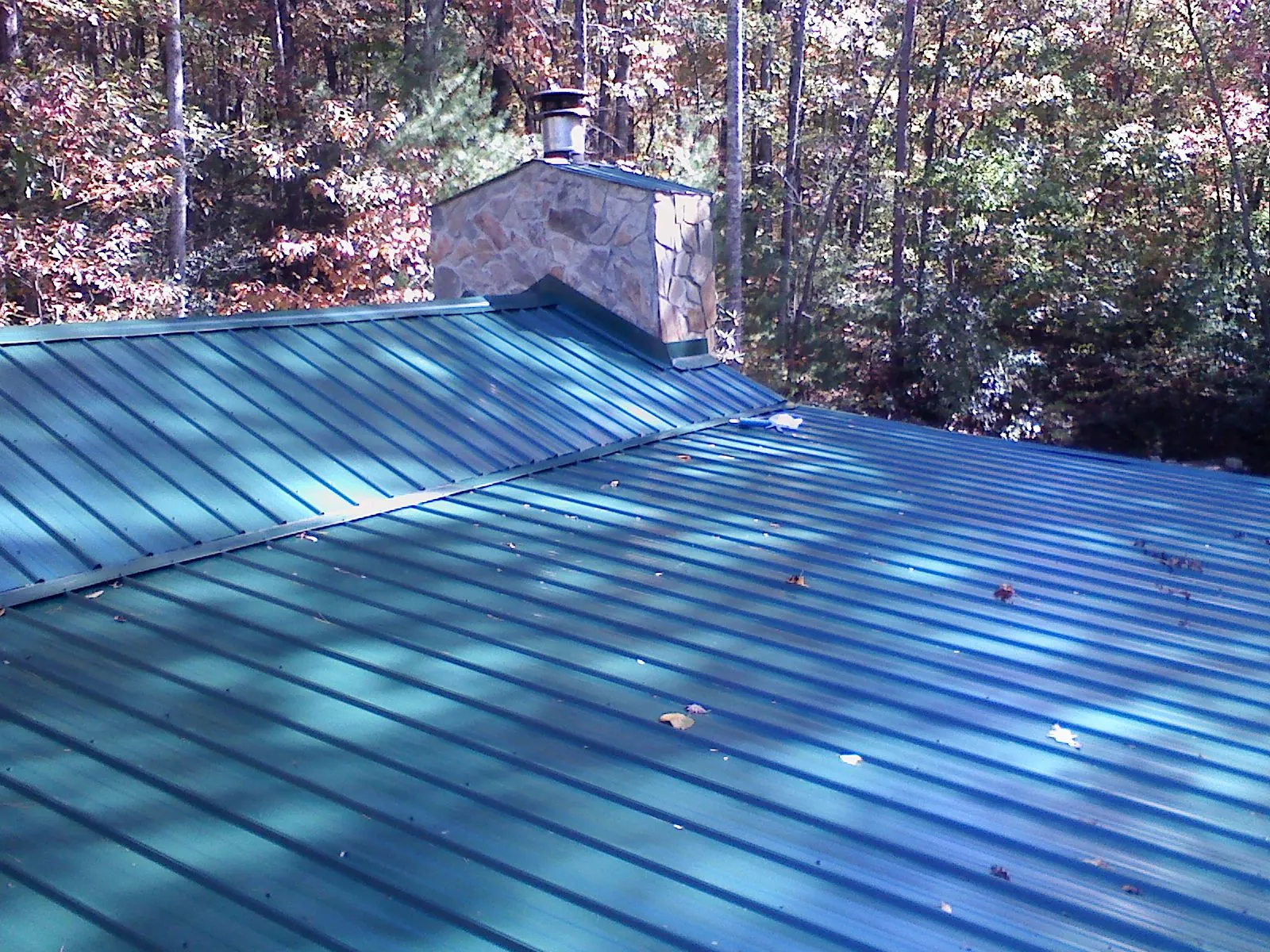 New green metal roof and stone chimney surrounded by autumn woods in Oak Park